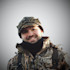 Smiling man in camouflage cap and jacket with black neck gaiter and backpack straps