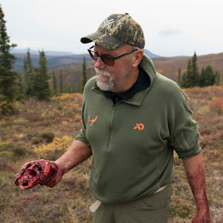 Man in glasses holding bloody animal heart, wearing green pullover with MeatEater and First Lite logos