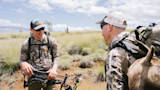 Two hunters in camouflage in grassland; one holds a compound bow; First Lite logo on shirt