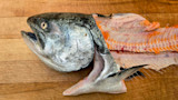 Salmon head and split fillets showing orange flesh on wooden cutting board