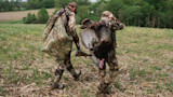 Two hunters carrying a wild turkey and gear through a harvested cornfield