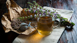 Glass mug of herbal tea with metal infuser, dried herbs on crumpled paper and fresh mint sprigs