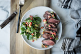 Cocoa-rubbed venison loin, sliced, with arugula salad, avocado and tomato on white plate