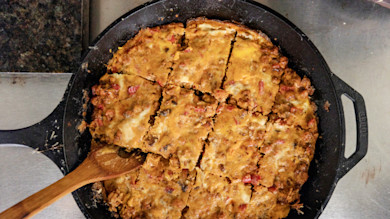 Skillet of baked crayfish casserole cut into squares with wooden spoon