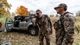 Two hunters by pickup; man aiming crossbow labeled 'SUB-1 XR' into field