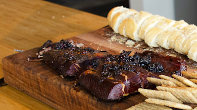 Blackberry-smoked salmon on wooden cutting board with sliced baguette and crackers