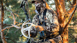 Hunter in camouflage holding shed antlers and compound bow in tree stand, MUDDY harness