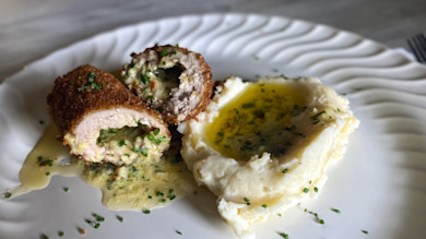 Two breaded stuffed meat rolls with creamy herb sauce and mashed potatoes in melted herb butter