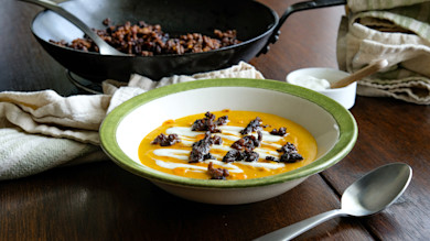 Smoked squash soup topped with chili venison sausage crumbles and sour cream drizzle in green-rim bowl