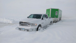 White RAM pickup stuck in deep snow towing green ice-fishing house on frozen lake