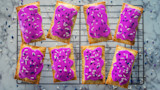 Rectangular pop‑tarts with bright purple icing and blue‑white sprinkles on a cooling rack