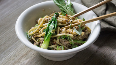 Stir-fried miso noodles with ground hog, bok choy, scallions, sesame and chopsticks in white bowl