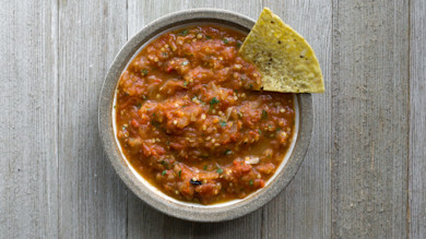 Bowl of chunky chiltepin salsa with a tortilla chip on a wooden table