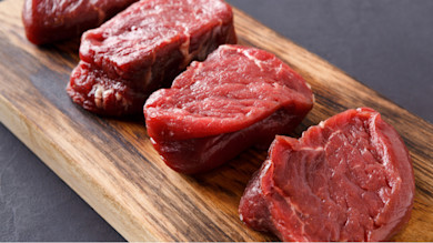 Four raw beef medallions on a wooden cutting board