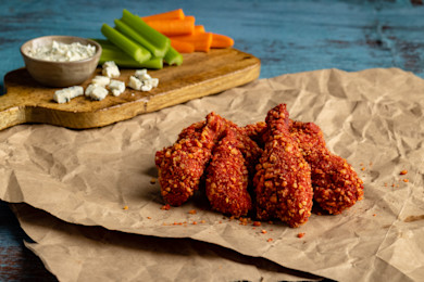 Bright red breaded pheasant drumsticks on brown paper with celery, carrots, and blue cheese dip