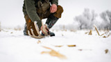 Hunter kneeling in snowy field picking up a frost-covered shed antler