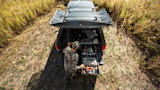 Hunter loading hunting gear into open pickup truck bed drawers in a grassy field