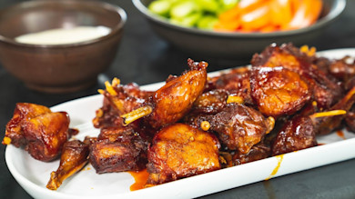 Sticky glazed meat bites on white platter, dipping sauce and vegetable bowl behind