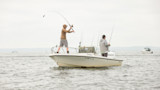 Two men fishing on a small white skiff, one casting a rod; outboard reads HONDA