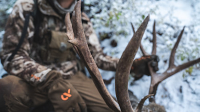 Mule deer antlers held by camo-clad hunter on snowy ground