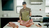 Man butchering a skinned deer quarter on a kitchen cutting board, holding a long boning knife