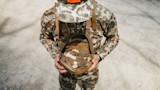 Hunter in camouflage holding open pouch containing several morel mushrooms