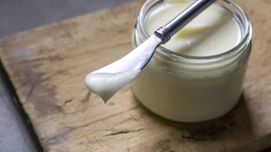 Jar of tallow-butter with knife holding a smear on wooden cutting board
