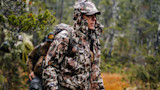 Hunter in camouflage rain jacket and cap carrying a backpack in a rainy forest