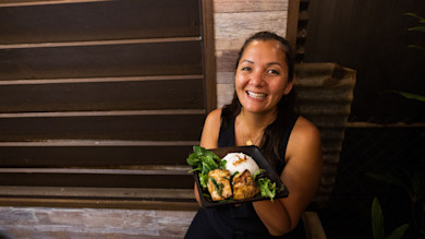 Smiling woman holding black plate with grilled marinated fish, rice, and greens