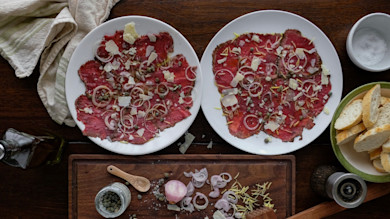 Two plates of venison carpaccio with shaved Parmesan, capers, shallot rings, and sliced bread