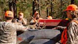 Hunters in orange caps gathered around pickup bed with deer antlers, truck decal "X4".