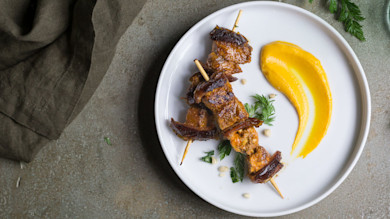 Turkey and date skewers with orange puree and parsley on a white plate