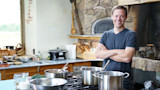 Steven Rinella smiling with arms crossed behind pots on a kitchen stove