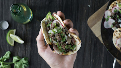 Hand holding lengua taco with chopped meat, radish, onion, cilantro