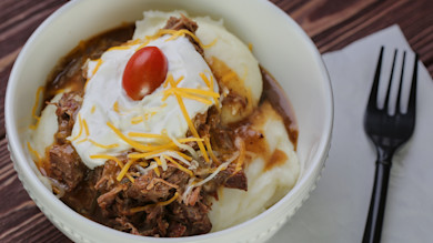 Mashed potatoes topped with shredded venison, gravy, sour cream, shredded cheddar, cherry tomato