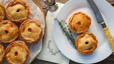 Venison beer hand pies on a wooden board and white plate with thyme sprig and carving knife