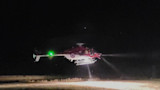 Helicopter hovering at night with spotlight illuminating ground, green navigation light