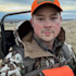 Man in orange hunting cap and camouflage jacket carrying a backpack in a grassy field