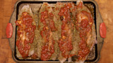 Baked catfish fillets on a sheet pan topped with tomato sauce, garlic cloves and herbs