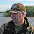 Man in camo jacket wearing cap reading "Field & Game" in shallow marsh