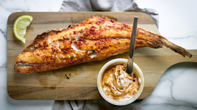 Grilled redfish on half shell with harissa yogurt and lemon on wooden cutting board
