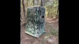 Camouflaged portable hunting blind with spray-painted graffiti and side window on forest trail