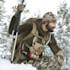 Hunter kneeling in snowy snow, wearing camo beanie with First Lite logo and backpack