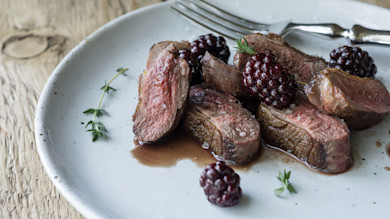 Seared duck breast slices with blackberry sauce and thyme on white plate