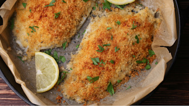 Breaded catfish fillets baked in skillet with parsley and a lemon wedge