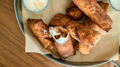 Fried turkey egg rolls on parchment-lined metal tray, one split open with dipping sauce