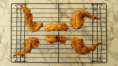 Six buttermilk-fried rabbit pieces on wire cooling rack over marble countertop