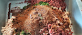 Ground meat with chopped onion, fat, herbs and a mound of spices in a gray tub