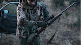 Hunter preparing a bolt-action rifle with scope, wearing camouflage jacket by open car door