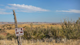 PRIVATE PROPERTY NO TRESPASSING sign on weathered fence post with open grassland and distant hills